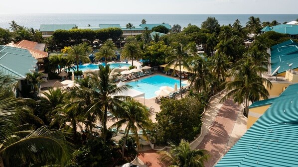 Ein Resort mit Schwimmbad, umgeben von Palmen und Liegestühlen, mit Blick auf ein Gewässer.