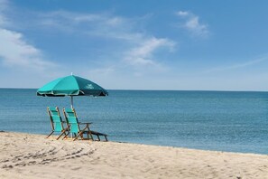 Ein Strand mit einem türkisblauen Sonnenschirm und zwei Holzstühlen.