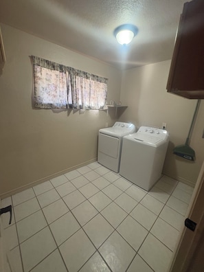 A laundry room with two washing machines, a window with floral curtains, and a ceiling light. - 3-bed 1 Bath; full washer and dryer; townhome; BBQ grill; nearby park (Las Cruces)
