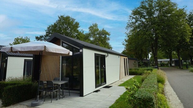 A modern outdoor seating area with a table and chairs under a canopy, adjacent to a building with glass doors. - Cozy Kaatsheuvel Chalet (Kaatsheuvel)