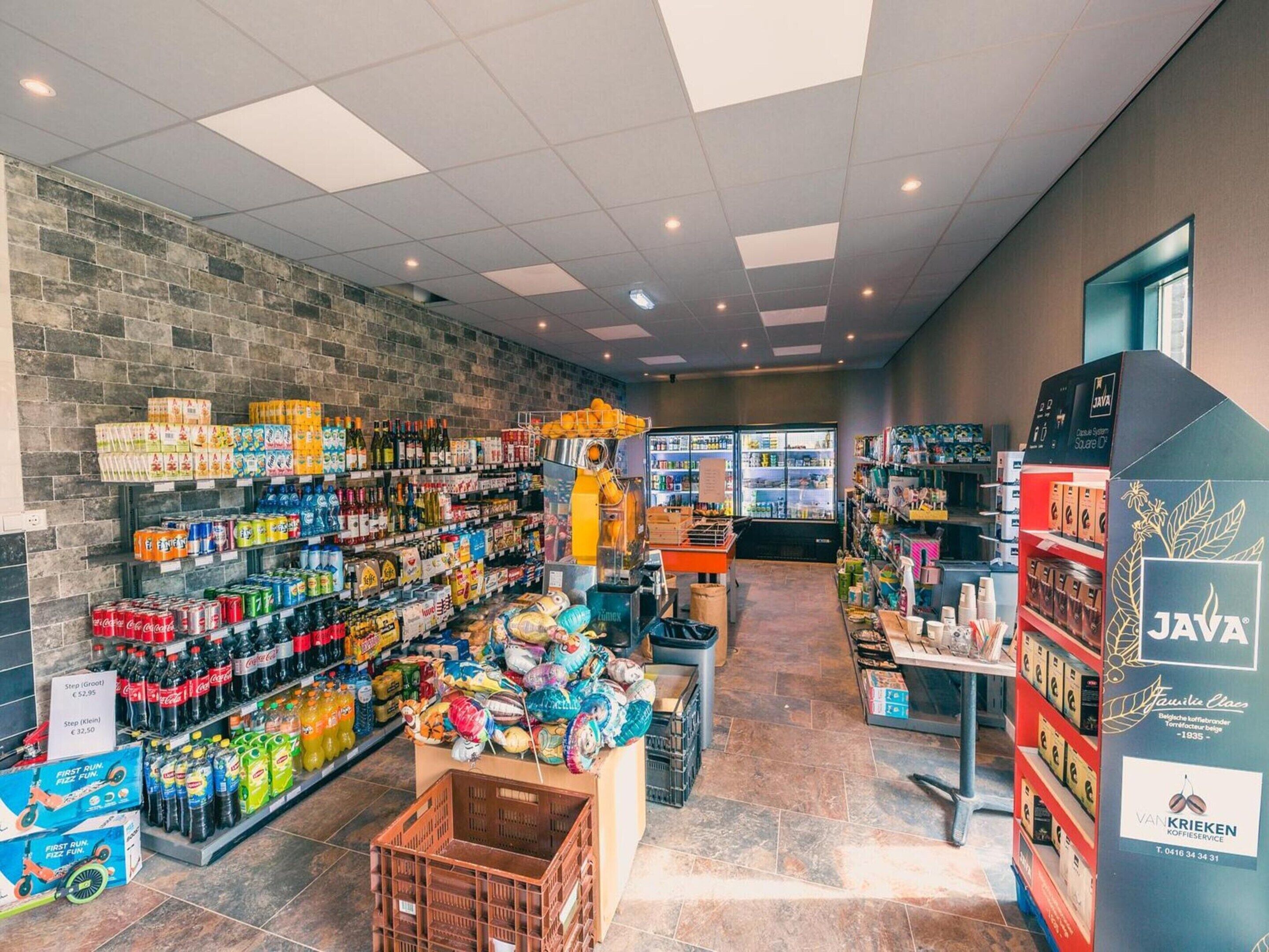 Ein Supermarktinneres mit Regalen voller Getränke, Snacks und einer Kühltheke.