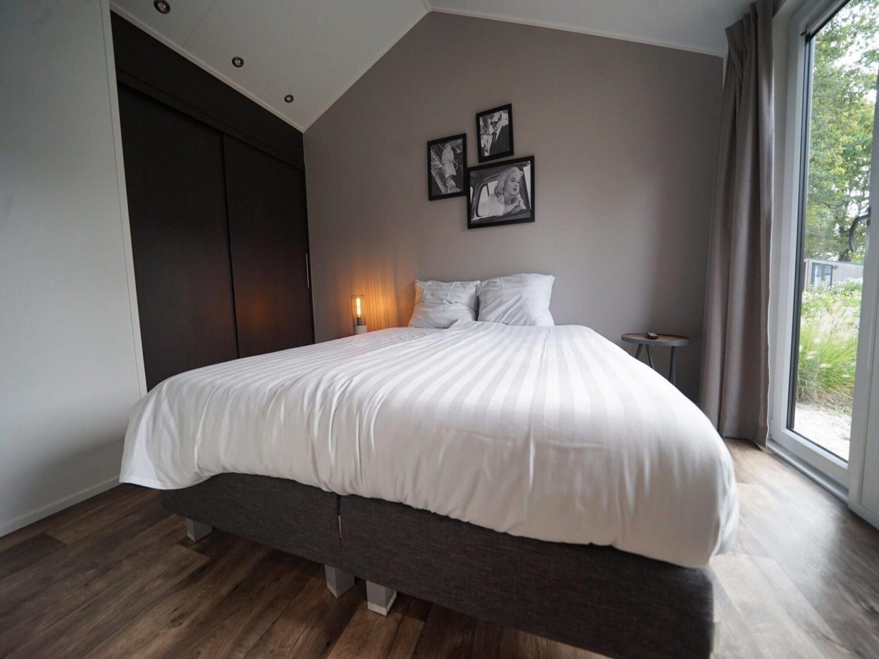 A modern bedroom with a large bed, a dark wardrobe, and a bedside table.