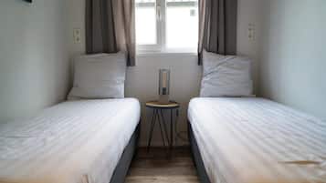 A small, clean room with two single beds, a small table, and a window with curtains.