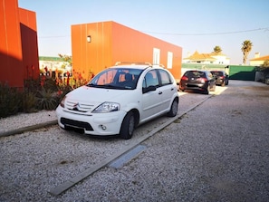 A white car parked on a gravel driveway with a red building in the background.