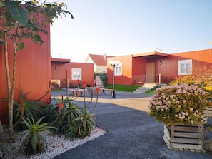 A building with a red exterior, a paved entrance, and a small garden area with plants and flowers.