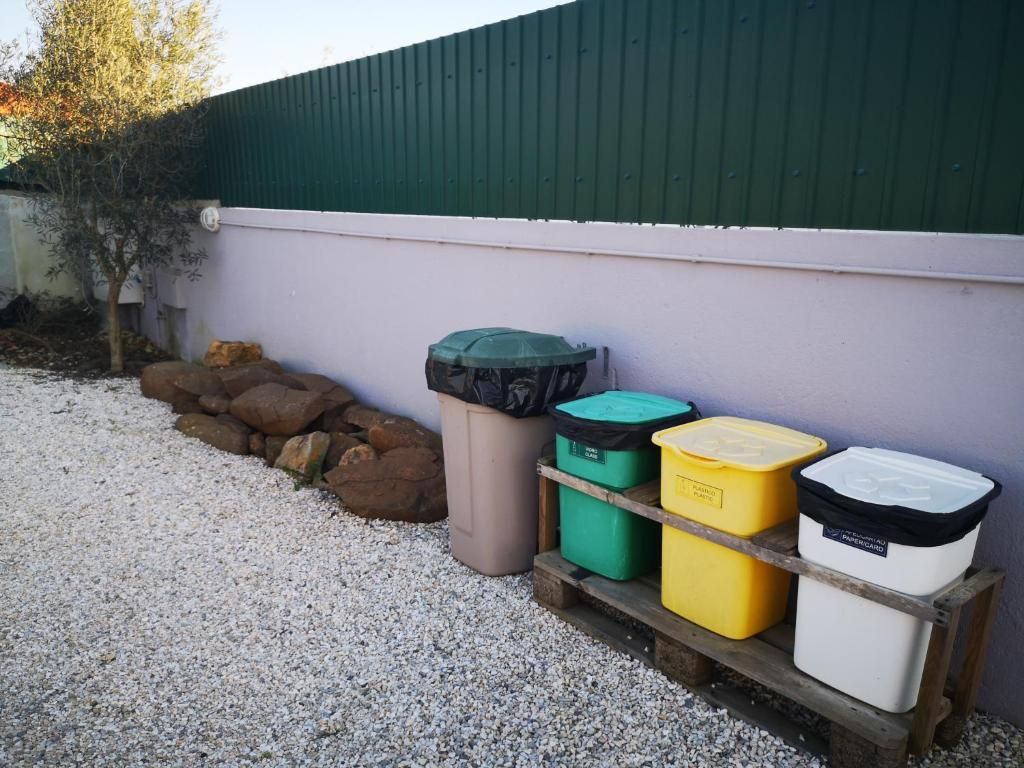 Latas de lixo ao ar livre sobre superfície de cascalho, adjacentes a um edifício com telhado verde.