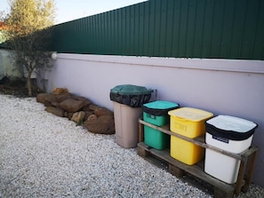 Outdoor waste bins on a gravel surface next to a building with a green roof.