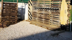 Une porte en bois, avec une planche de surf appuyée contre, une clôture et un mur vert en arrière-plan.