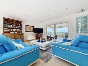 A modern living room with a large bookshelf, a flat-screen TV, and a view of the outdoors through a sliding glass door. - Luxury 4-Bedroom Villa in Saint-Tropez with Panoramic Sea Views (Saint-Tropez)