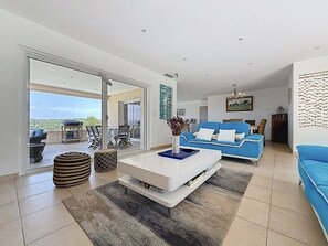 Un salon moderne doté d’une grande porte-fenêtre coulissante donnant sur un balcon, d’un canapé bleu, d’une table basse blanche et d’un tapis à motifs.