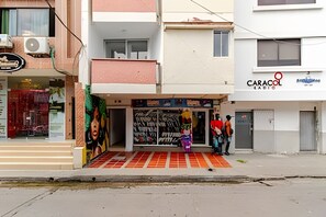 Vista de calle con un edificio que tiene escaparates, un mural colorido y un cartel que dice 'CARACOL RADIO'.