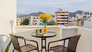 Un balcón con dos sillones de mimbre, una mesa redonda pequeña y un florero con flores amarillas.