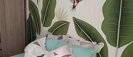 Un dormitorio con cama, almohadas y una pared decorada con motivos de hojas.