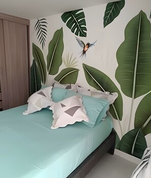 Un dormitorio con cama, almohadas y una pared decorada con motivos de hojas.