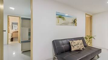 A modern living room with a leather sofa, a framed artwork on the wall, and a view into the adjacent bathroom.