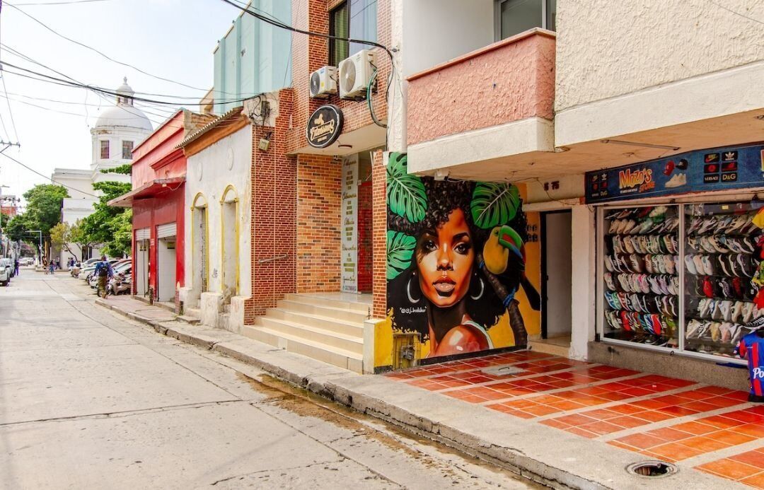 A street with buildings, one with a mural of a woman's face and a shoe store.