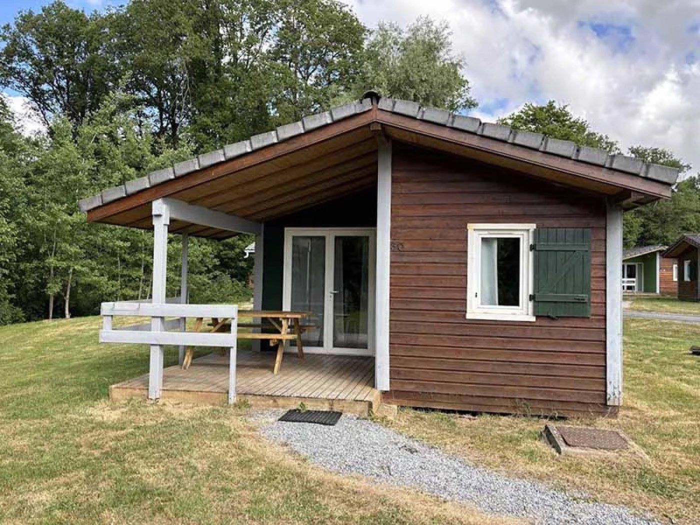 Een klein houten vakantiehuisje met een veranda, een deur en een raam met luiken.
