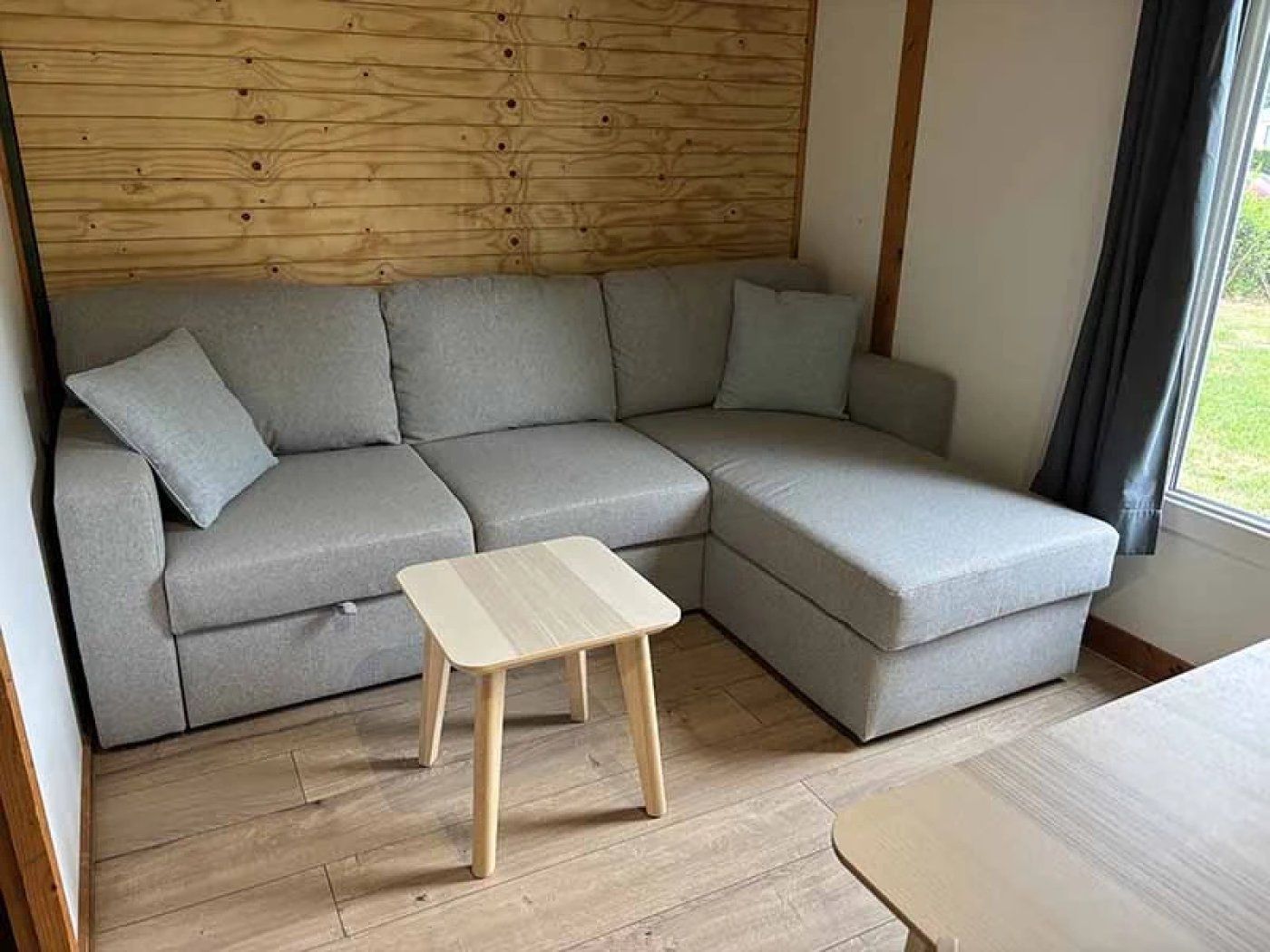 Een moderne woonkamer met een grijze modulaire bank, een kleine houten salontafel en een houten hoofdbord.