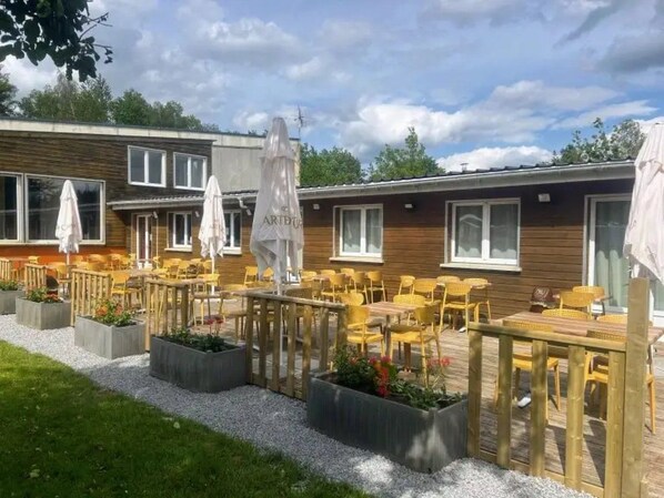 A patio area with outdoor seating and umbrellas, surrounded by wooden deck and planters.