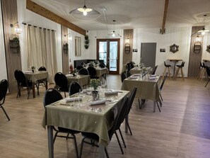 A dining area with tables set for service, wooden beams on the ceiling, and a view of the street through the door.
