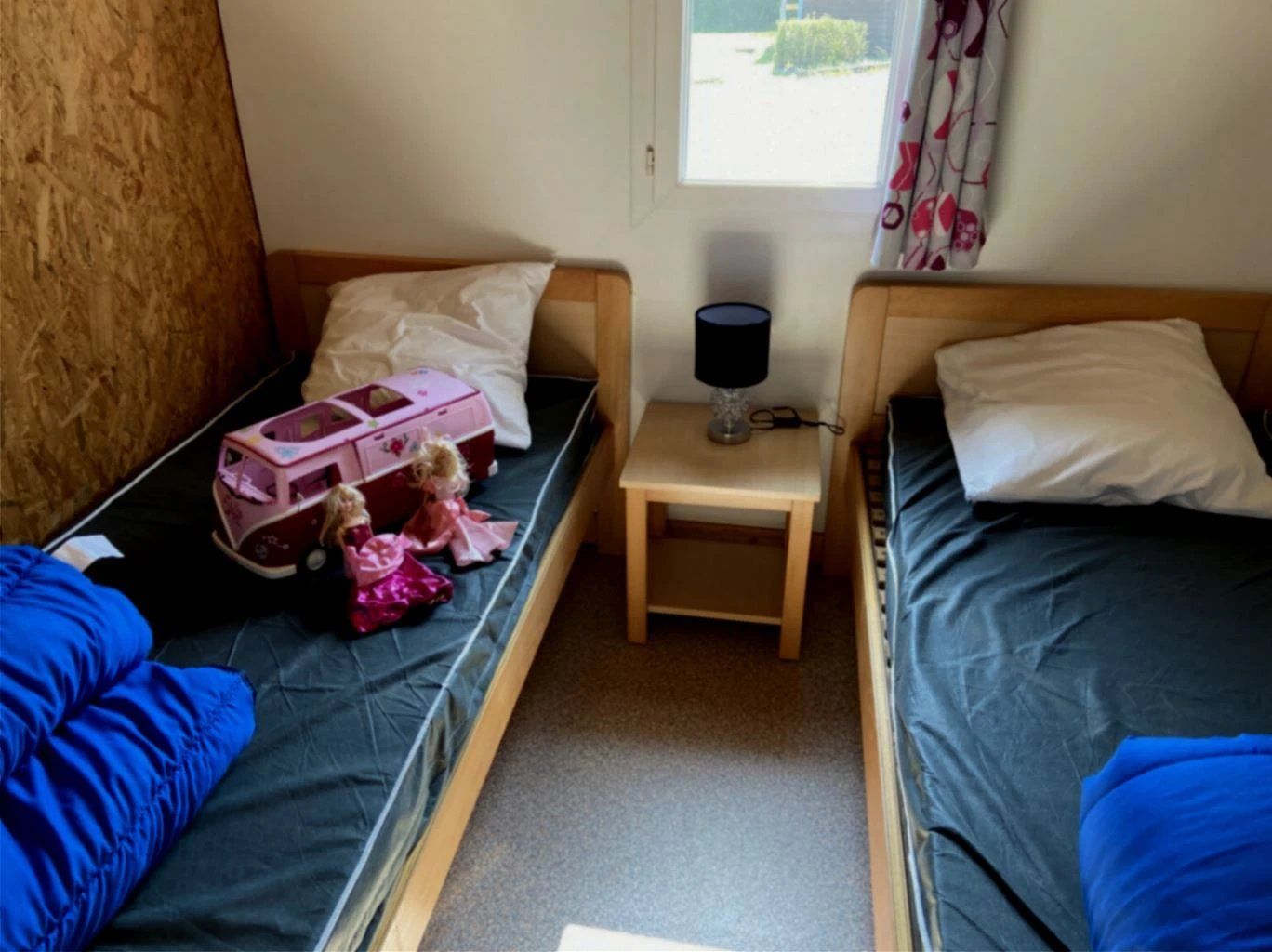 Une chambre avec deux lits simples, une petite table avec une lampe et une fenêtre avec des rideaux.