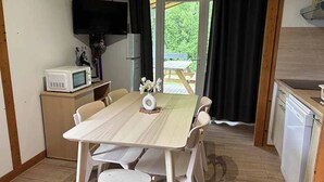 A compact kitchen with a dining table, chairs, a microwave, a refrigerator, and a television mounted on the wall. - Chalet 4 étoiles - Piscine  - ccbgdbf (Signy-le-Petit)