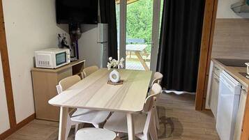 Une cuisine compacte comprenant une table à manger, des chaises, un four à micro-ondes, un réfrigérateur et un téléviseur fixé au mur.