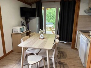 A compact kitchen with a dining table, chairs, a microwave, a refrigerator, and a television mounted on the wall.