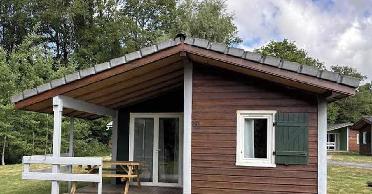 Een klein houten vakantiehuisje met een veranda, een schuifpui en een bankje.