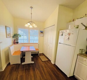 Uma cozinha compacta com mesa de jantar, armários brancos, uma geladeira e um lustre.