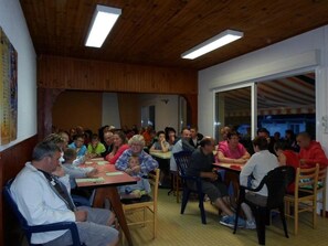 Eine Gruppe von Personen sitzt an Tischen in einem Raum mit Holzwänden und einer geneigten Decke.