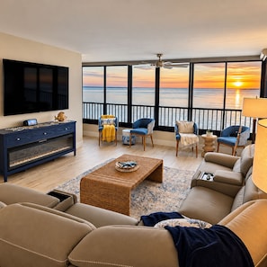A living room with a large TV, comfortable seating, a coffee table, and a view of the sunset over the ocean. - Premium Luxury Top-Floor Bayside Penthouse (Fort Myers)