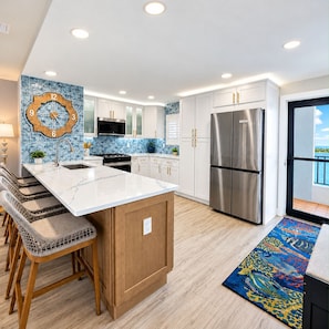A modern kitchen with white cabinets, stainless steel appliances, and a large island with bar stools. - Premium Luxury Top-Floor Bayside Penthouse (Fort Myers)