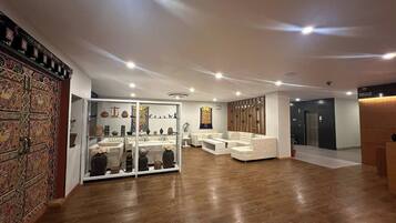 Um hall amplo com design moderno, apresentando um painel de vidro com objetos decorativos, área de estar com sofás e painel de parede em madeira.