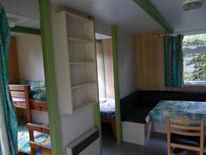 Habitación pequeña con literas, una mesita y ventana con cortinas.