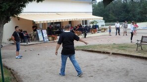 Ein Essbereich im Freien mit Tischen und Stühlen, ein überdachter Sitzbereich und ein Gebäude im Hintergrund.