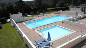 Piscina com duas áreas distintas, rodeada por espreguiçadeiras e guarda-sóis.