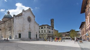 Un edificio histórico con cúpula y campanario, rodeado por una plaza con banderas y algunas personas.