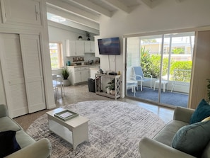 A living room with a sofa, a coffee table, and a TV. There is a kitchen area with cabinets and a dining table. - Casa Mar 11 - Standard Plus (Siesta Key)