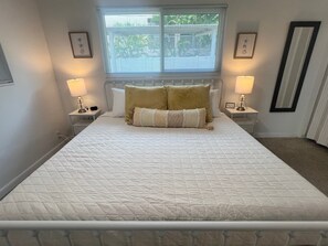 A neatly made bed with a quilted bedspread and two pillows, flanked by bedside tables with lamps, in a room with a window and framed pictures on the walls. - Casa Mar 11 - Standard Plus (Siesta Key)