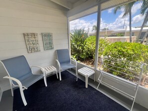 A covered seating area with two chairs and a small table, a dark carpet, and two wall decorations with inspirational quotes. - Casa Mar 11 - Standard Plus (Siesta Key)