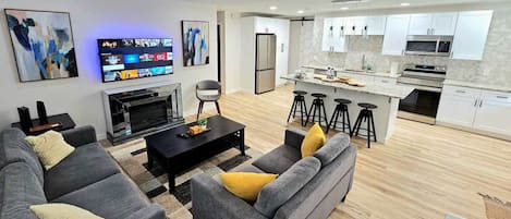 A modern living room with a flat-screen TV, grey sofas, a coffee table, and a fireplace.