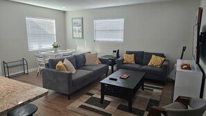 A living room with two sofas, a coffee table, a TV, and a dining area with a table and chairs. - 4BR Port Tampa Retreat Fenced Yard Patio (Tampa)
