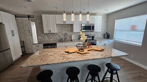 A modern kitchen with a central island, bar stools, and pendant lighting. - 4BR Port Tampa Retreat Fenced Yard Patio (Tampa)