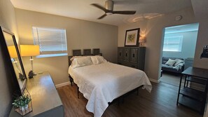 A bedroom with a bed, a ceiling fan, a nightstand with a lamp, a dresser, and a window with blinds. - 4BR Port Tampa Retreat Fenced Yard Patio (Tampa)