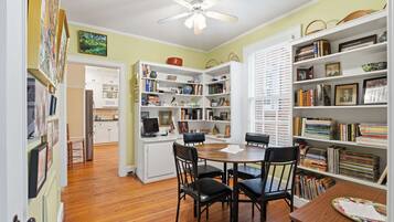 A room with a dining table, chairs, a ceiling fan, and bookshelves filled with books and decorative items.