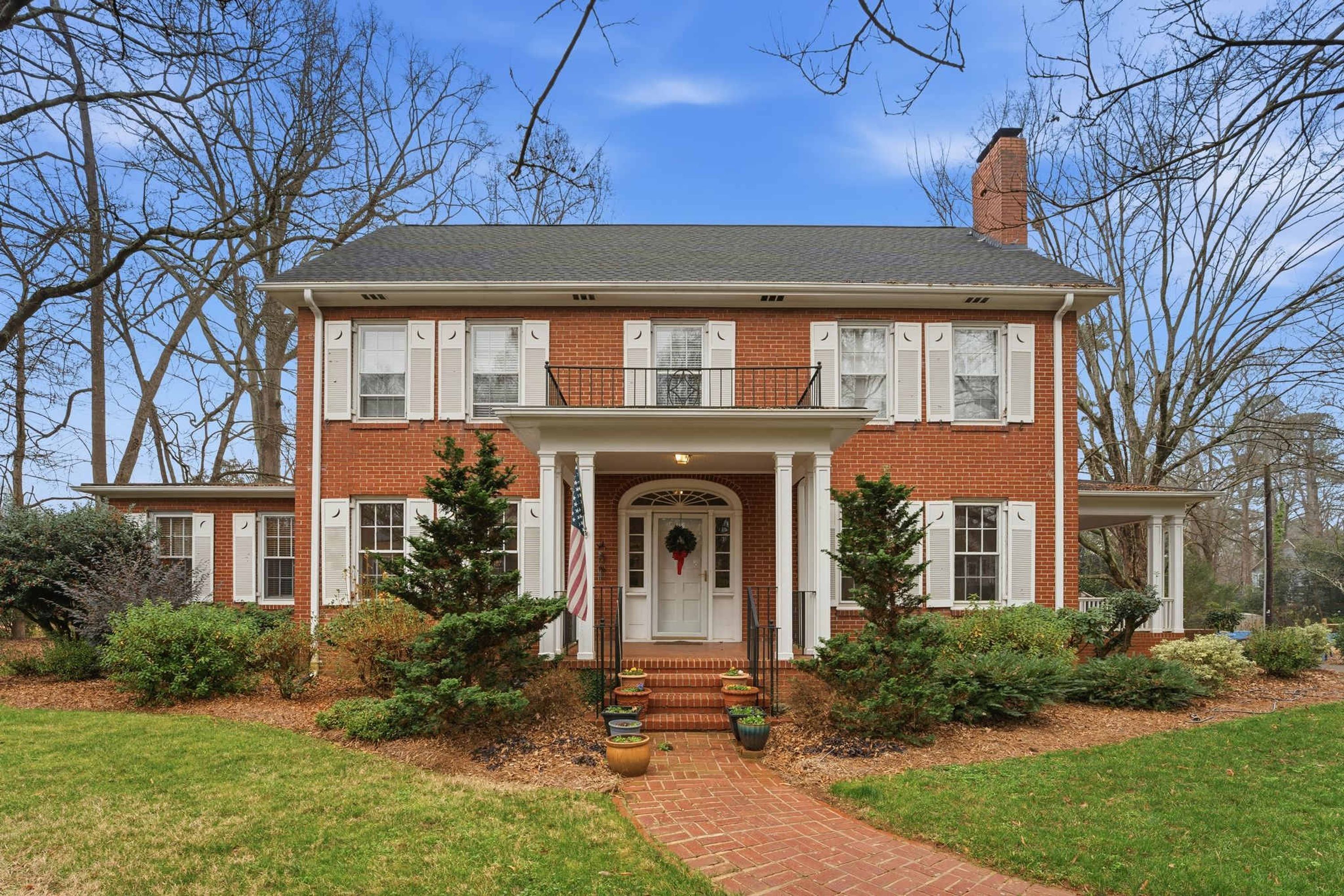 A two-story brick house with a front porch, a chimney, and a well-maintained lawn.