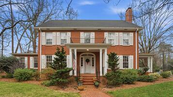 A two-story brick house with a front porch, a chimney, and a well-maintained lawn.
