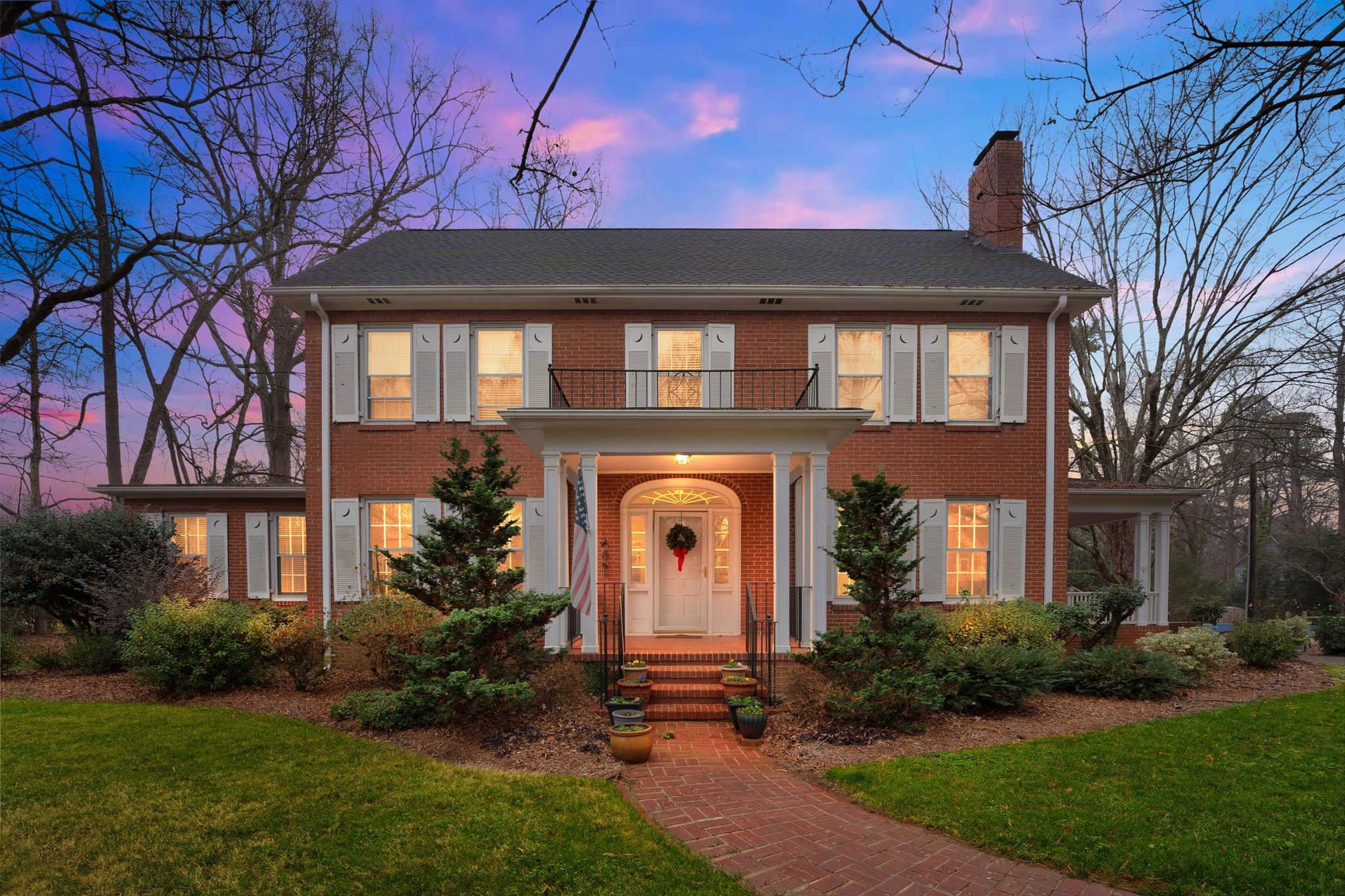 A two-story brick house with a front porch, a flag, and a wreath.