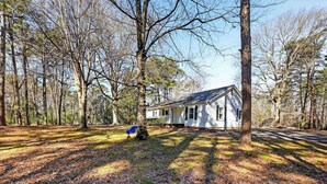 A single-story house with a gabled roof, surrounded by a forested area with leaf-covered ground. - Cozy 3BR Cottage Sauna Minutes to Davidson (Mooresville)